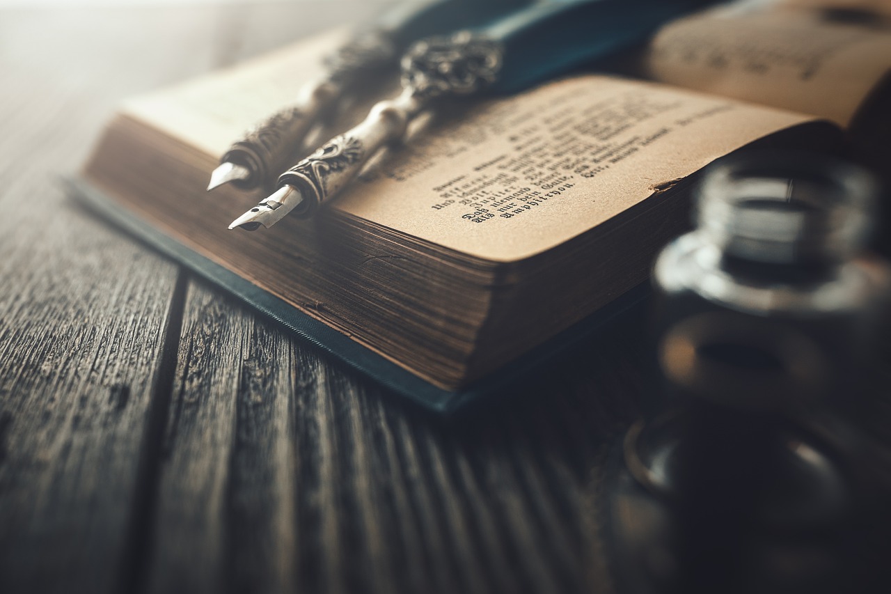 Antikes Buch mit verzierten Schreibfedern, liegend auf einem Holztisch, symbolisiert das Schreiben und Literatur.