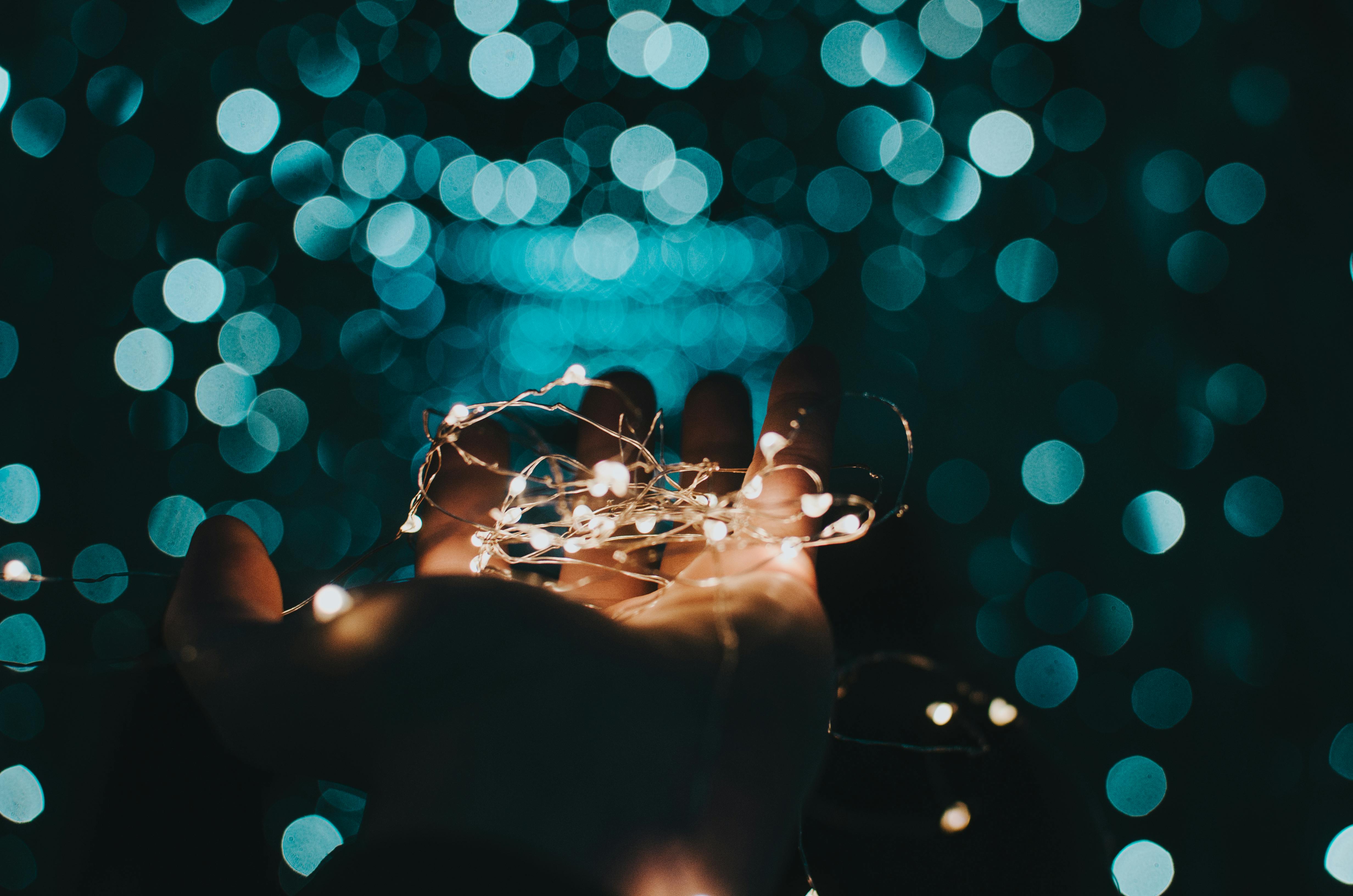 Hand hält eine leuchtende Lichterkette vor einem Hintergrund aus blauen Bokeh-Lichtern.