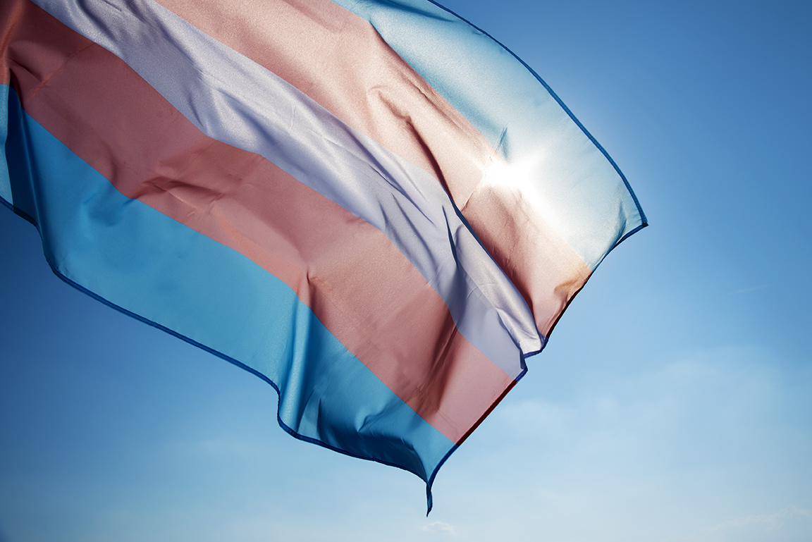 Transgender-Flagge weht im Wind vor einem klaren blauen Himmel.